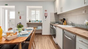 Eine moderne Küche mit Holzarbeitsplatte, Geschirrspüler und Spüle. Ein Esstisch mit einer Schale Gebäck und einer Topfpflanze.