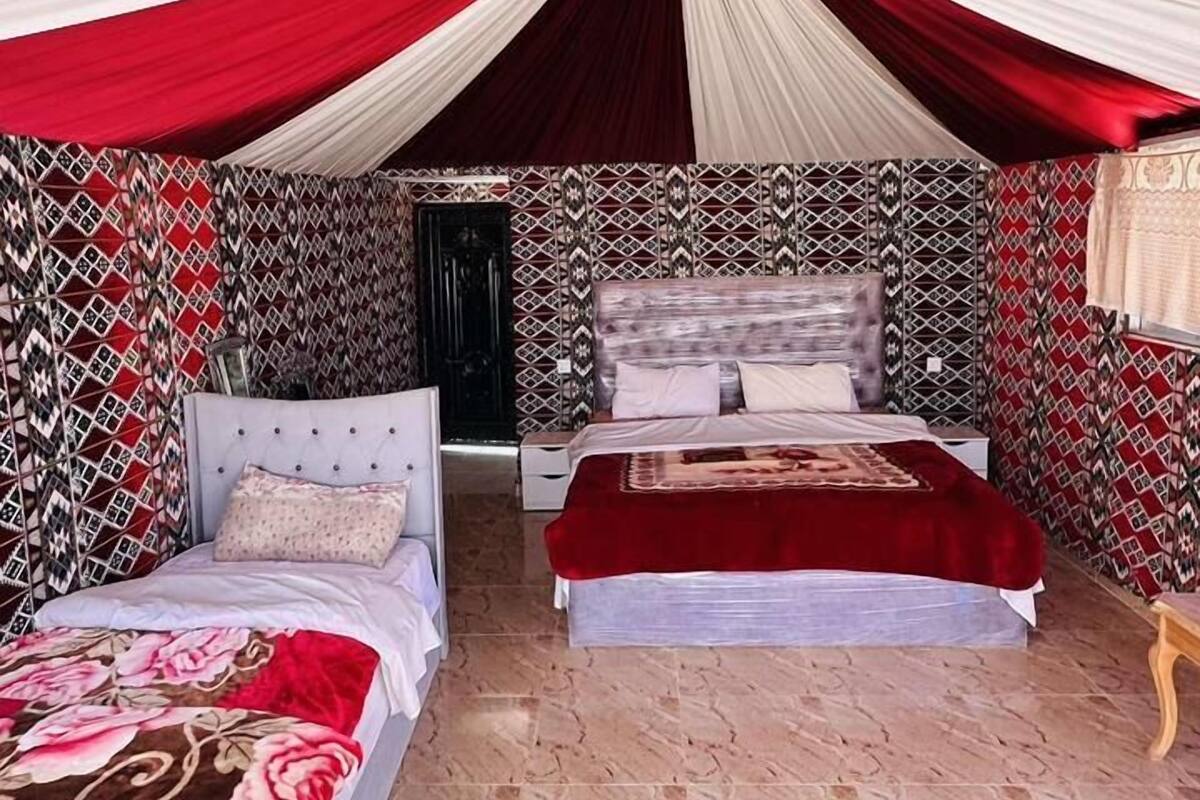 A room with two beds, patterned walls, and a red and white draped ceiling.