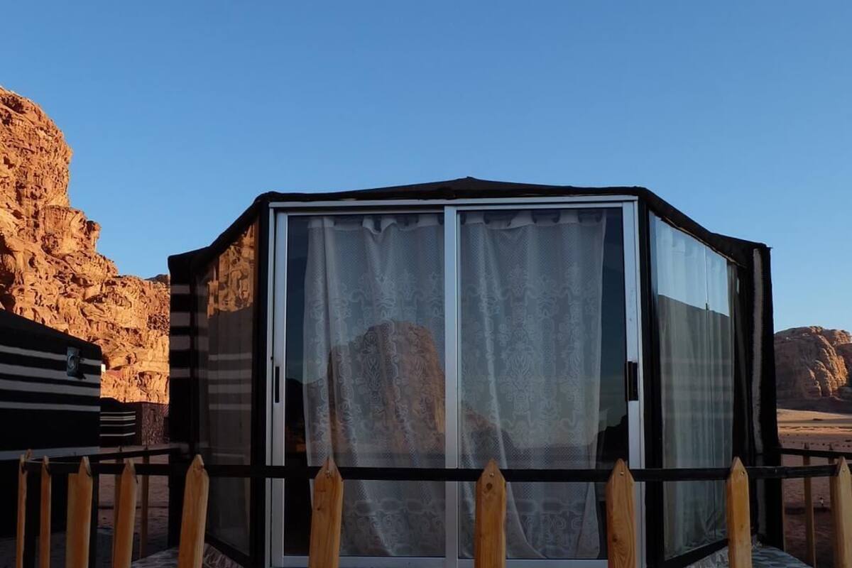A glass-enclosed structure with a metal frame, a tiled floor, and a wooden fence.