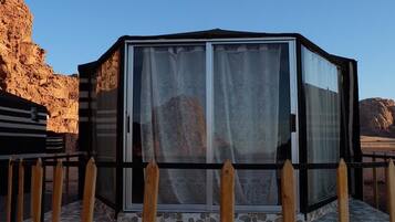 A glass-enclosed structure with a metal frame, a tiled floor, and a wooden fence.