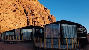 Une série de cabanes modernes aux murs de verre et aux garde-corps en bois, construites au pied d’une vaste formation rocheuse.