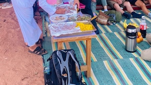 Un groupe de personnes s’est réuni autour d’une table où étaient disposés de la nourriture et des boissons. Ils étaient assis sur un tapis rayé à l’extérieur, avec un paysage rocheux en arrière-plan.