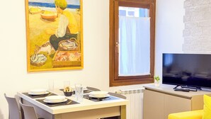 A dining area with a table set for four, a television, and a painting of a beach scene. - C A L I by Ca-sa Check (Chioggia)