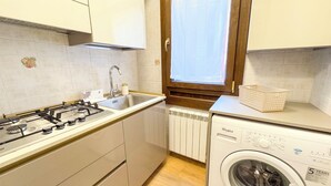 A compact kitchen with a gas stove, sink, and a built-in washer-dryer unit. - C A L I by Ca-sa Check (Chioggia)