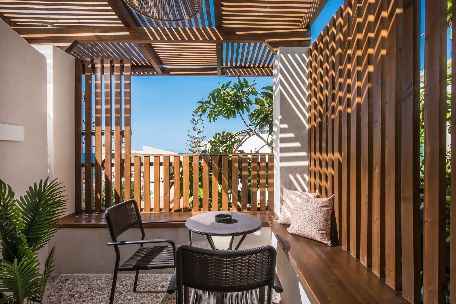 Une terrasse extérieure avec une clôture en bois, une table ronde, deux chaises et un banc doté de coussins.