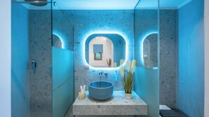 Une salle de bain moderne avec un grand miroir, un lavabo rond et un espace douche.