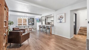 A spacious living area with a wooden floor, a brown leather sofa, and a dining area with bar stools. - Spacious Retreat 8 Bedroom River (Bethany)