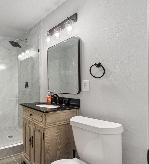 A modern bathroom with a glass shower enclosure, a vanity with a sink, a toilet, and a large mirror with lights. - Spacious Retreat 8 Bedroom River (Bethany)