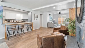 A modern kitchen with white cabinets, a wooden island with bar stools, a dining area with leather chairs, and a fireplace with a mirror. - Spacious Retreat 8 Bedroom River (Bethany)