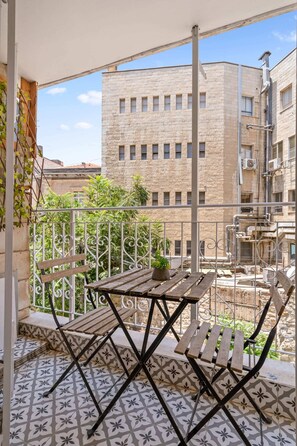 Ein Balkon mit Holztisch und -stühlen, einem gemusterten Boden und Blick auf ein Gebäude mit zahlreichen Fenstern.