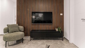 A modern living room with a flat-screen TV mounted on a wooden panel wall, a black entertainment unit with a plant, and a green upholstered armchair.