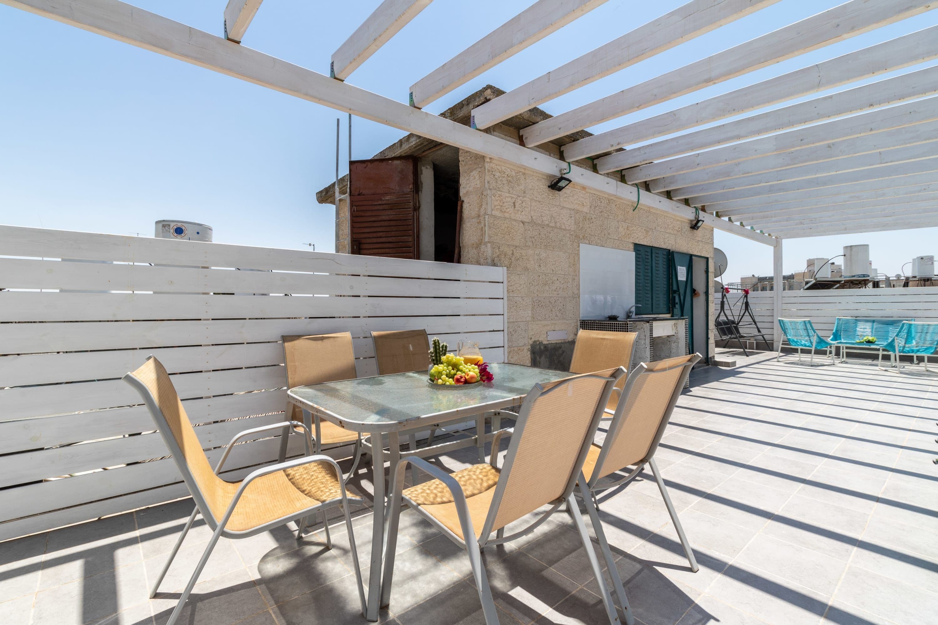An outdoor patio with a table and chairs, a white pergola, and a view of the cityscape.