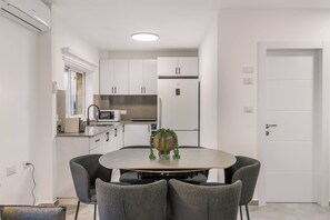 A modern kitchen with white cabinets, a stainless steel refrigerator, and a dining table with four chairs.