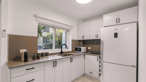 A modern kitchen with white cabinets, a built-in microwave, a stainless steel refrigerator, and a window with a view of the outside.