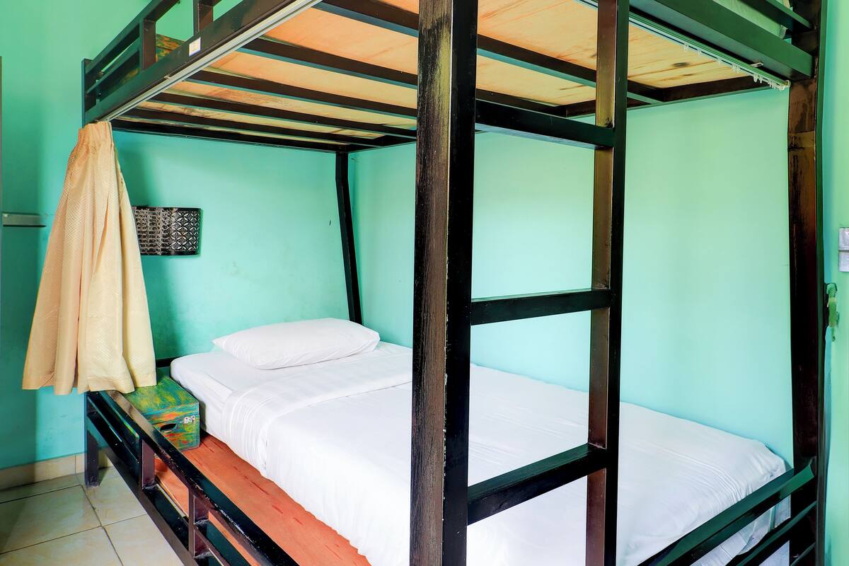 A bunk bed with a wooden frame and white bedding, a green wall, and a small shelf with a box.