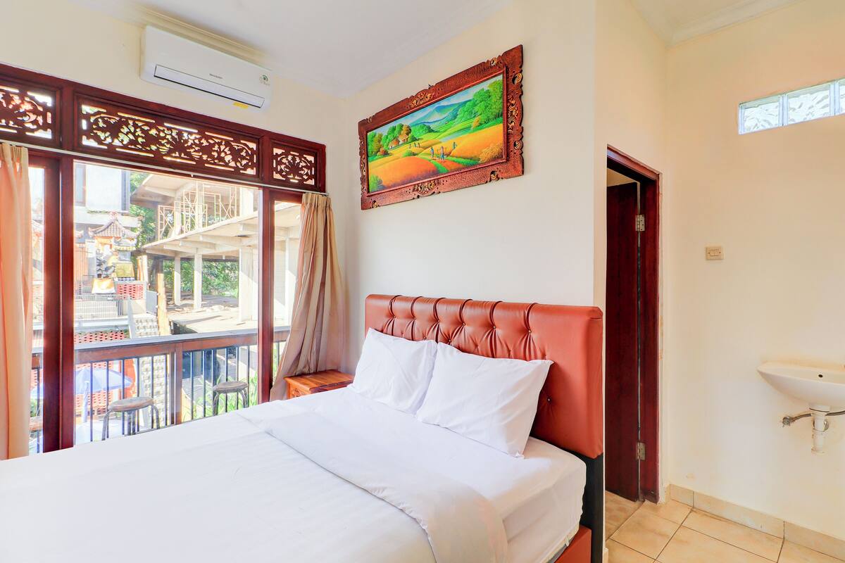 A hotel room with a bed, a painting, a window with a view, and a bathroom with a sink.