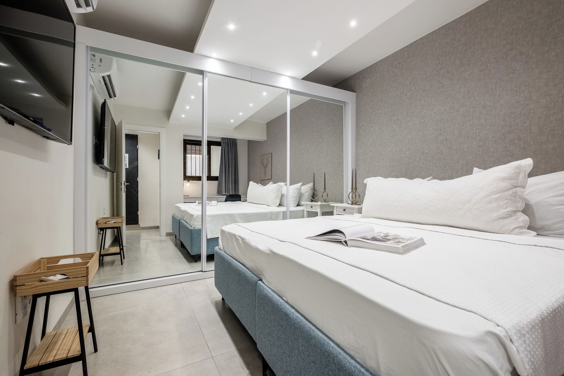 A modern hotel room with a large bed, a TV, a mirror, and a small seating area.
