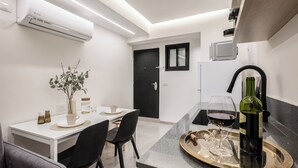 A modern kitchen with a dining area, featuring a white table, black chairs, a small plant, and a wine bottle on a tray. - baraca boutique (Jerusalem)
