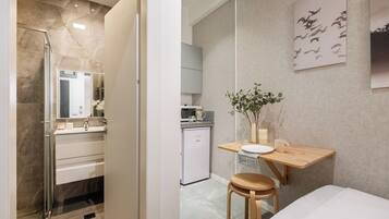 A modern bathroom with a glass shower enclosure, a vanity with a mirror, and a small seating area with a table and a stool.