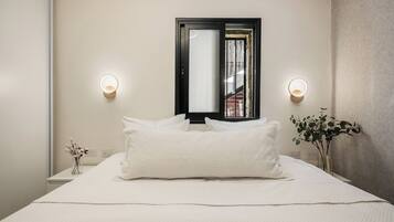 A neatly made bed with white linens, two bedside tables with lamps, a mirror above the bed, and a potted plant on the right side.