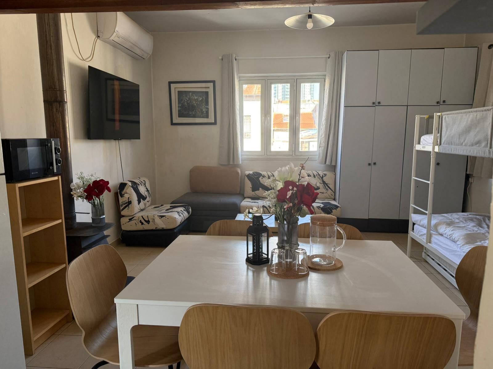 Un espacio habitable compacto con una mesa de comedor, sillas, un sofá, un televisor, una kitchenette y una cama plegable.