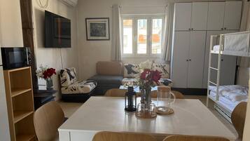 Un espacio habitable compacto con una mesa de comedor, sillas, un sofá, un televisor, una kitchenette y una cama plegable.