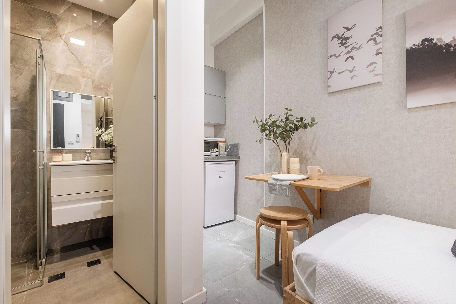 A modern bathroom with a shower, a sink, and a mirror. There is a small wooden table with a plant and a candle.