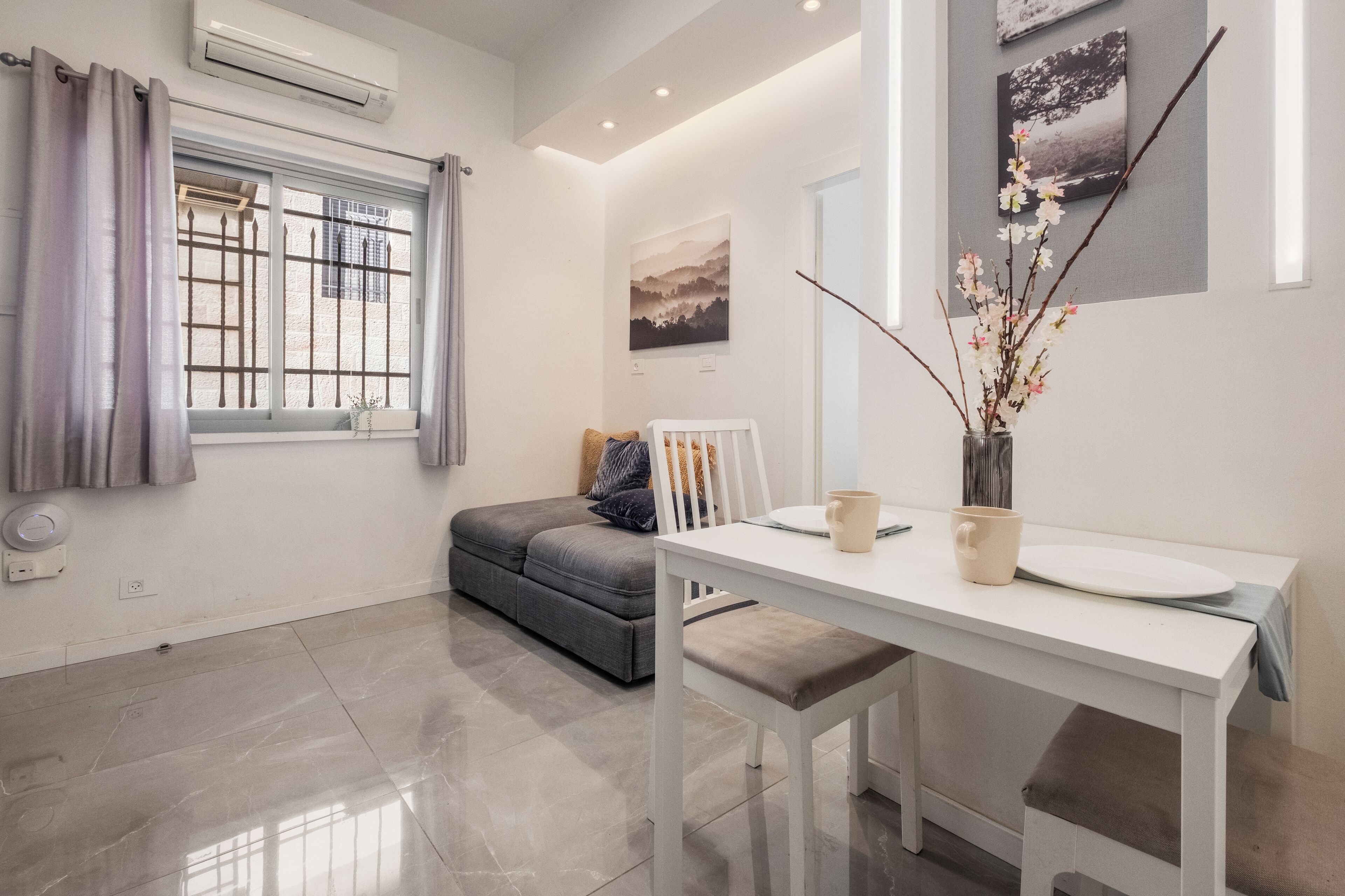 A modern room with a white dining table, grey sofa, and a window with curtains.