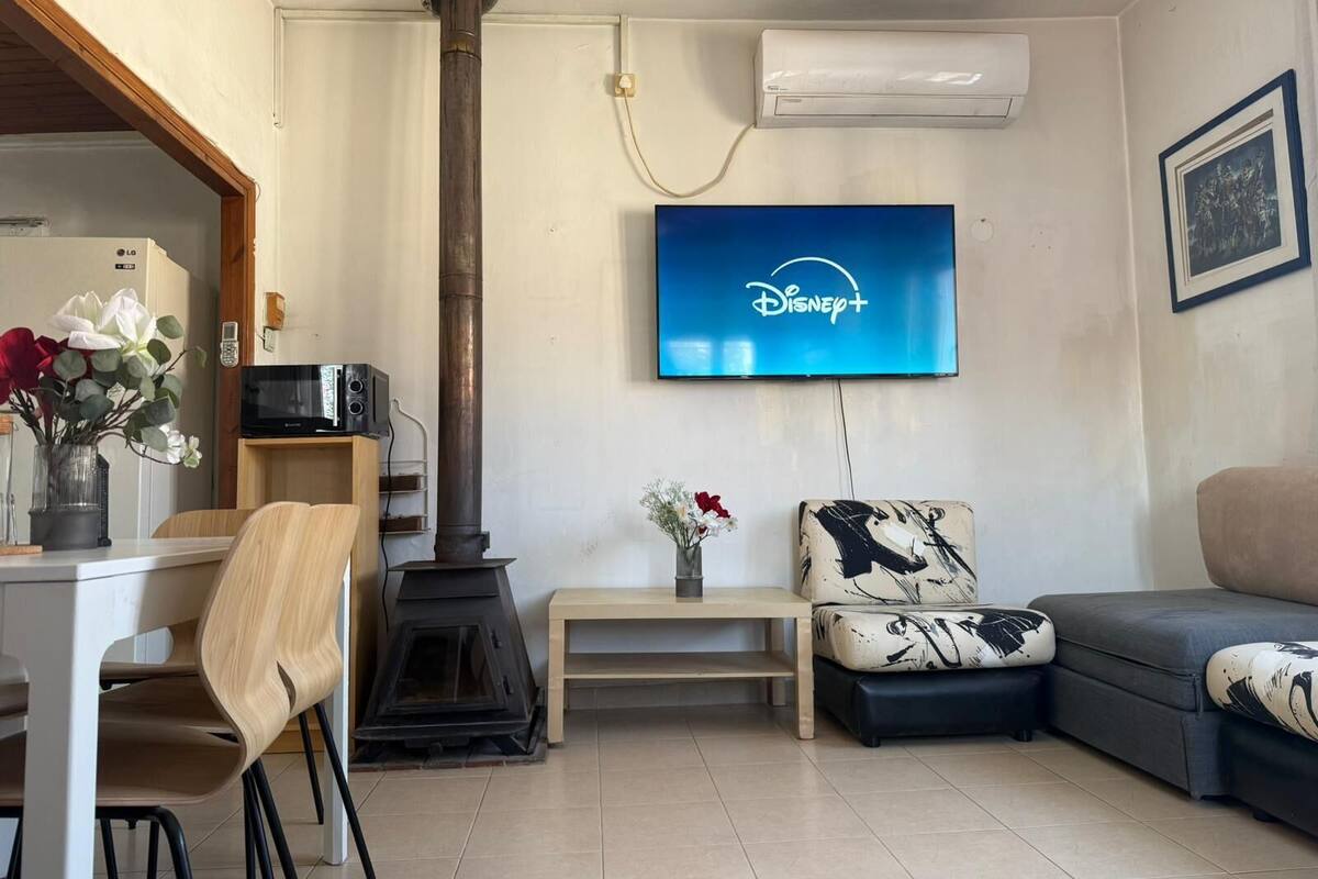 Uma sala de estar com lareira, uma TV de tela plana na parede, um sofá e um espaço de jantar com uma cadeira e uma mesa.