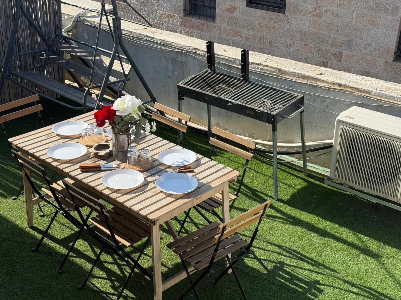 Un comedor al aire libre con una mesa de madera preparada para cuatro personas, rodeada de sillas.