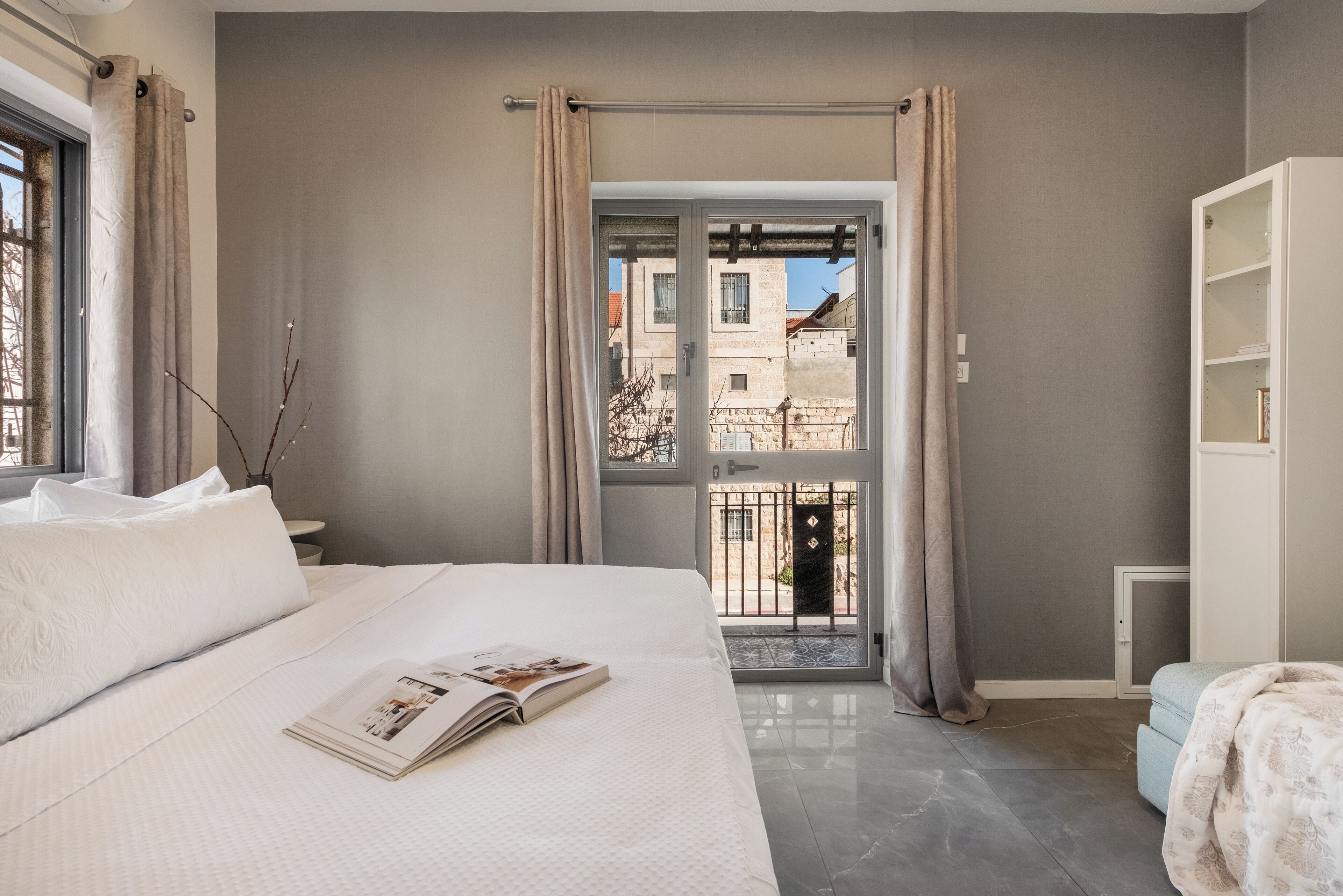 Ein Schlafzimmer mit einem Bett, einem Fenster, einer Tür zu einem Balkon und einem weißen Kleiderschrank.