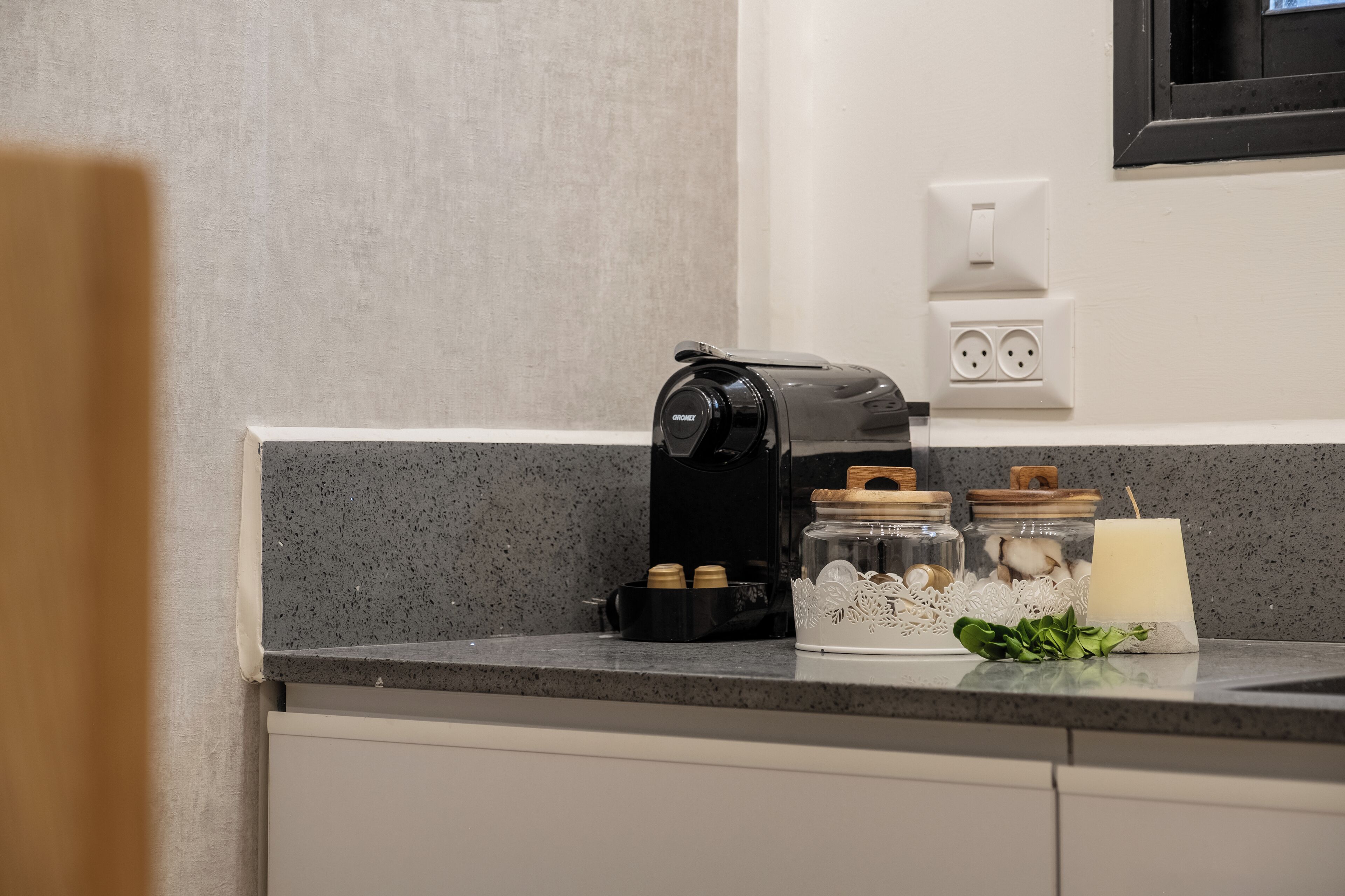 A kitchen counter with a coffee maker, jars, and a candle.