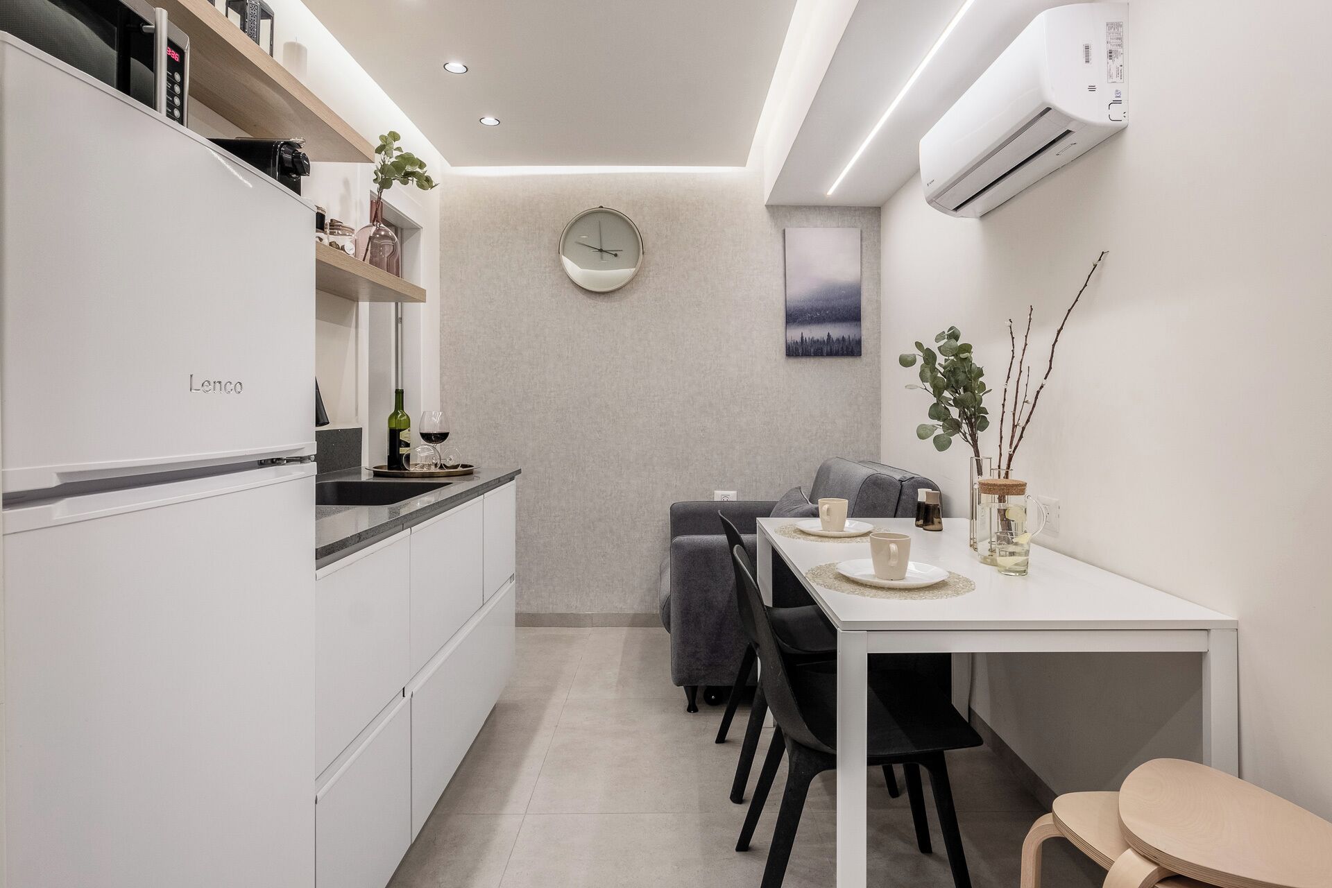 Una cocina moderna con un refrigerador Lenco, un comedor con mesa y sillas, y un reloj fijado en la pared.