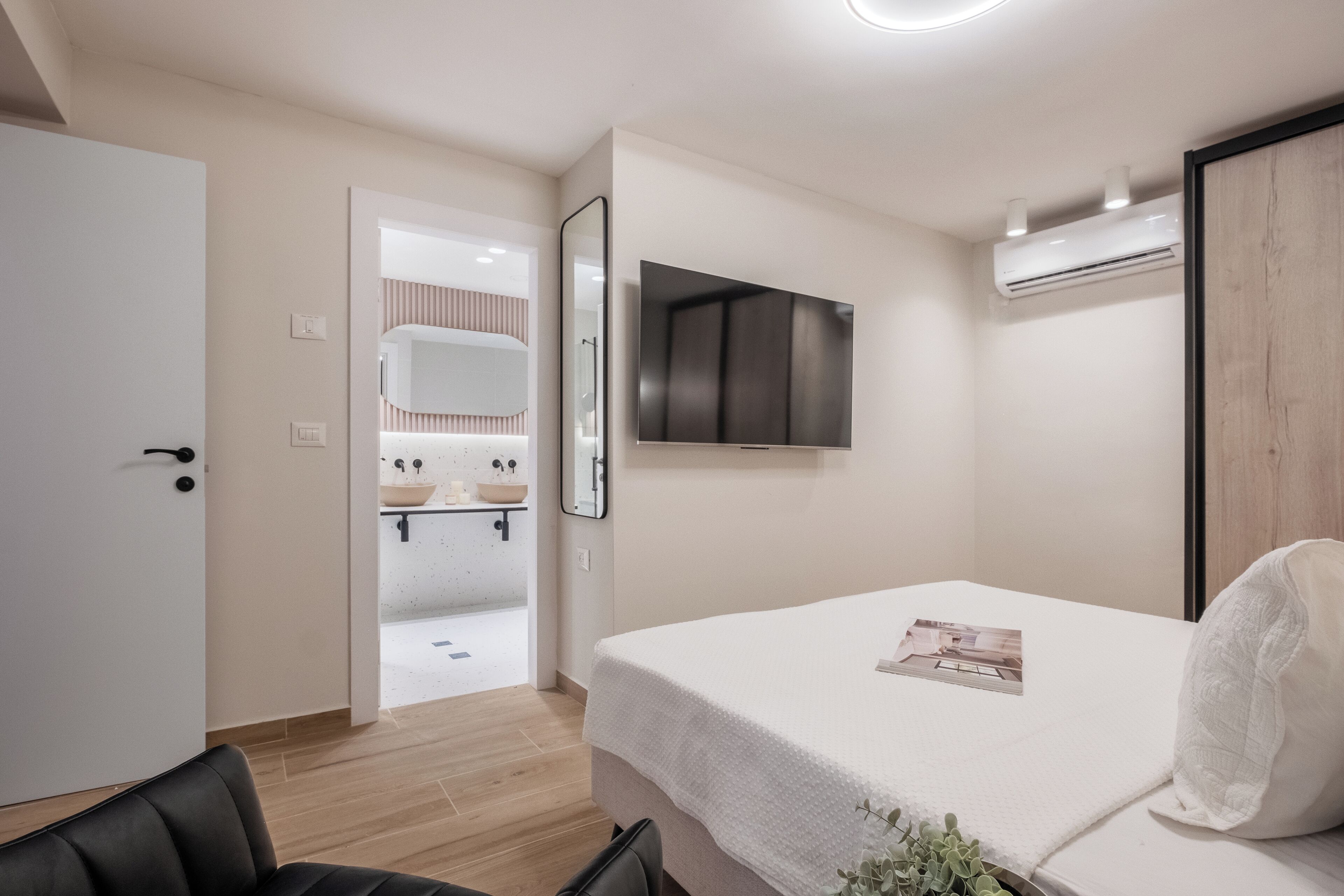 Een moderne hotelkamer met een bed, een aan de muur bevestigde televisie, een airconditioning en een badkamer die door een open deur zichtbaar is.
