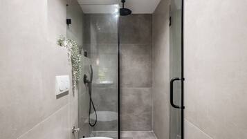 Un baño moderno con cabina de ducha de vidrio, inodoro y grifo empotrado en la pared.