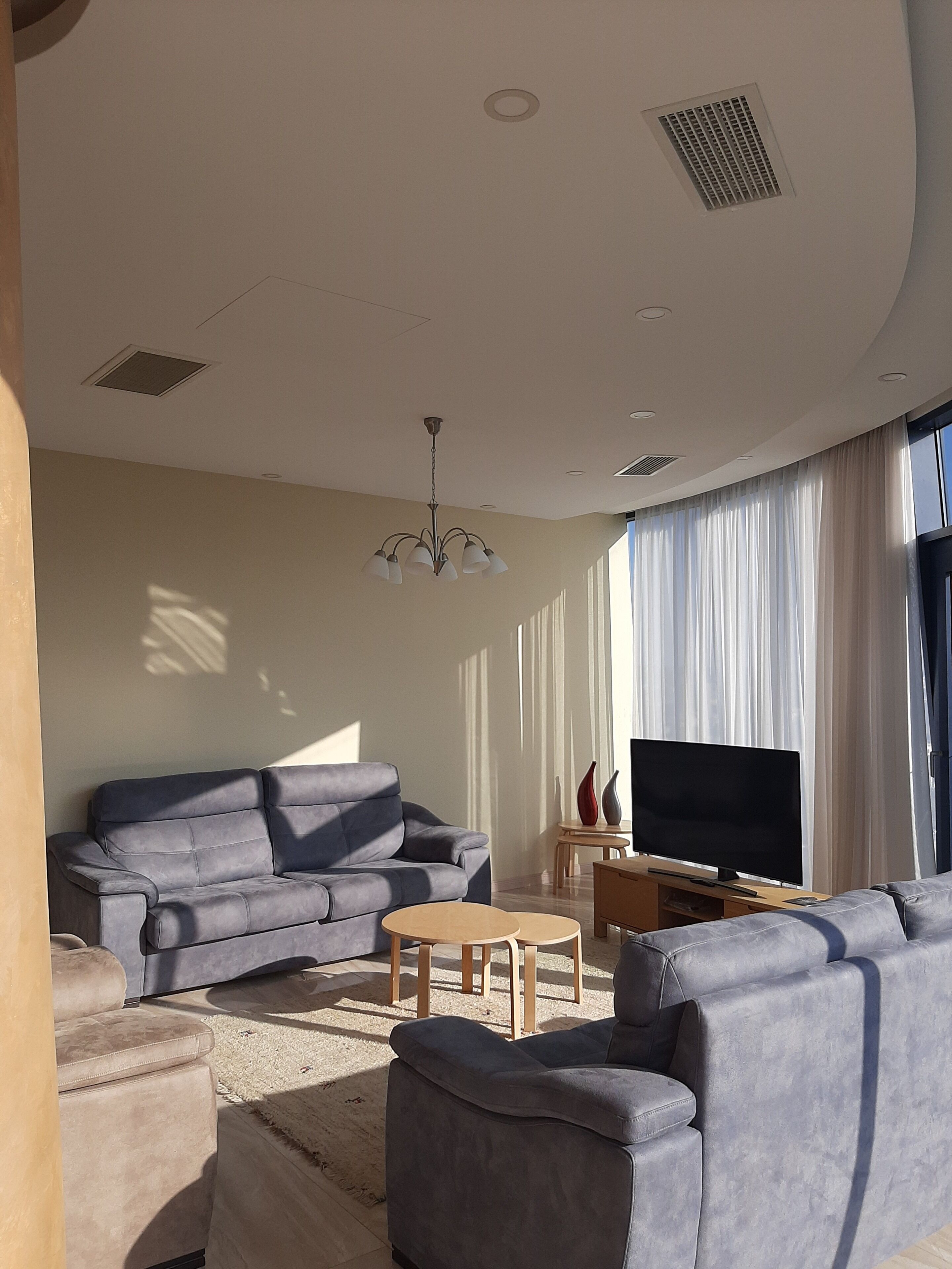 A modern living room with a grey sofa, a TV, and a chandelier.