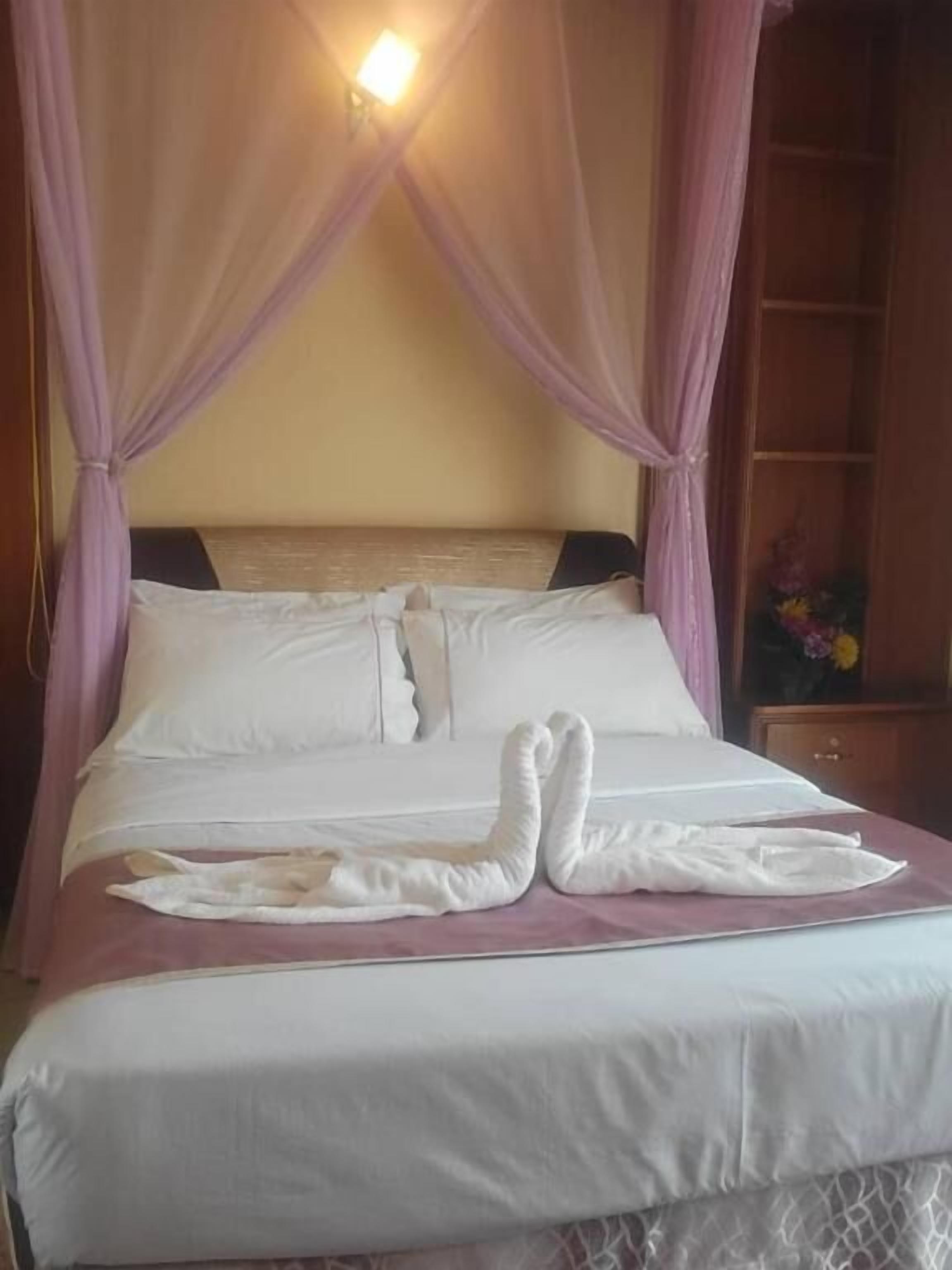 A neatly made bed with a canopy, a bedside table, and a nightstand with a vase of flowers.
