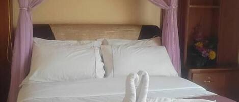 A neatly made bed with a canopy, a bedside table, and a nightstand with a vase of flowers.