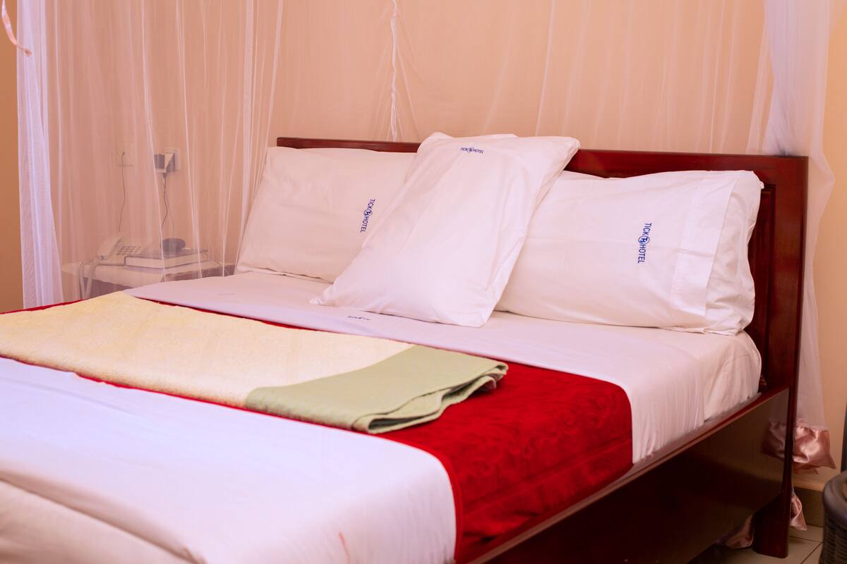 A neatly made bed with white linens, a red blanket, and a mosquito net.