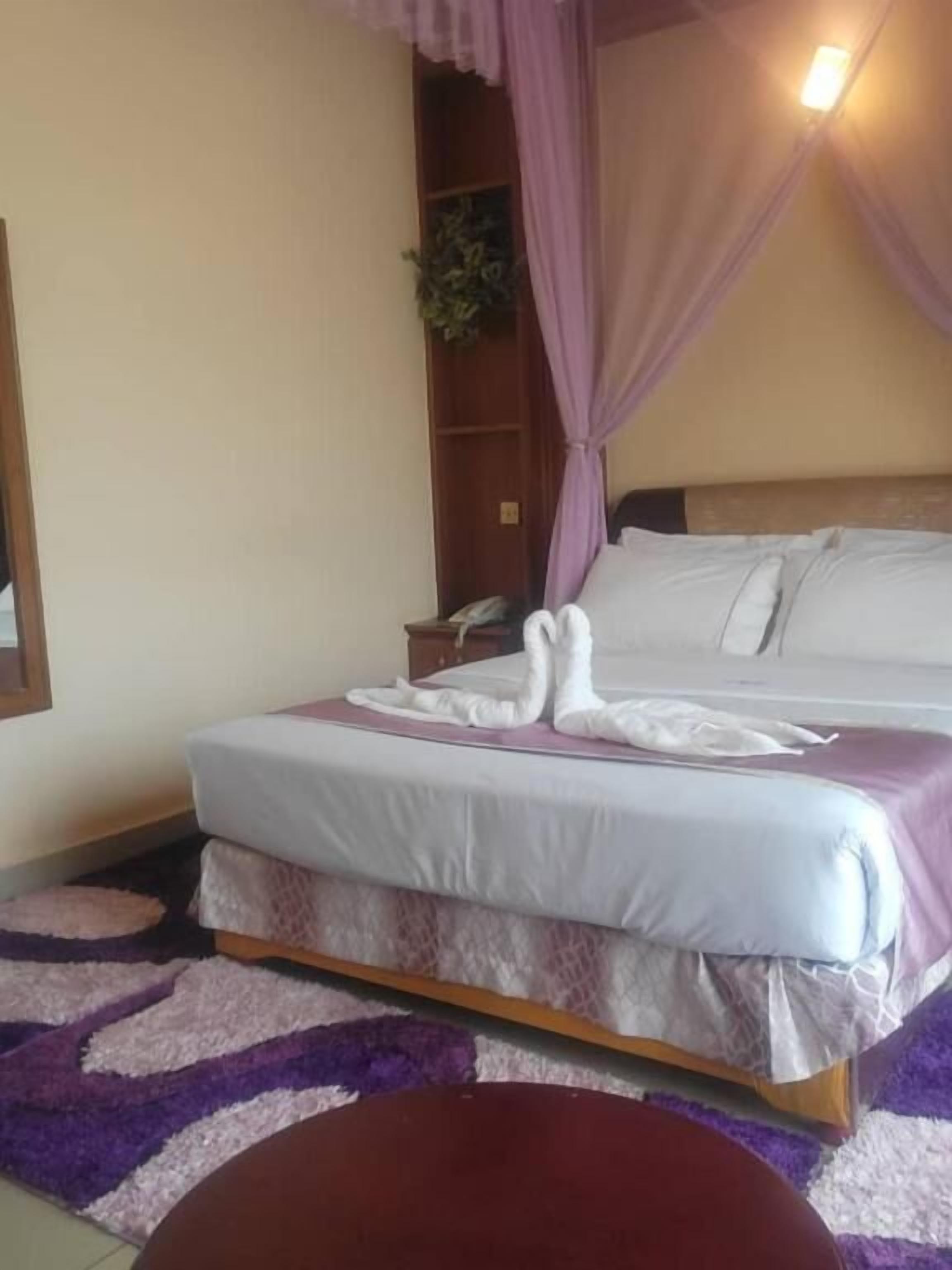 A hotel room with a bed, a bedside table, a telephone, and a small plant.