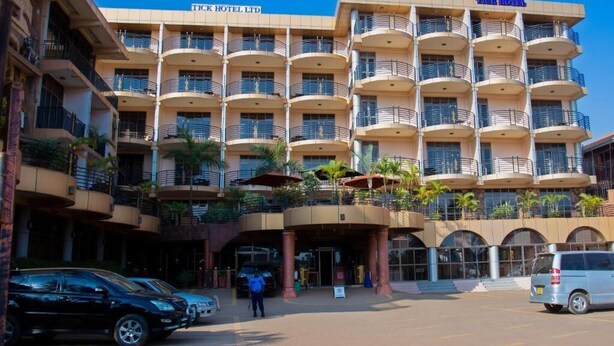 A multi-story hotel with balconies, a central entrance, and a parking area. - Tick Hotel (Kampala)