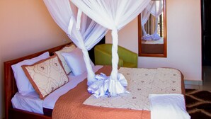 A bed with a canopy, pillows, a blanket, and a bedside table. - Tick Hotel (Kampala)