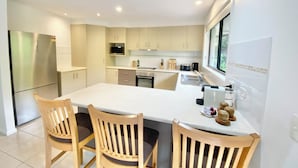 A modern kitchen with a central island, wooden chairs, and a stainless steel refrigerator.