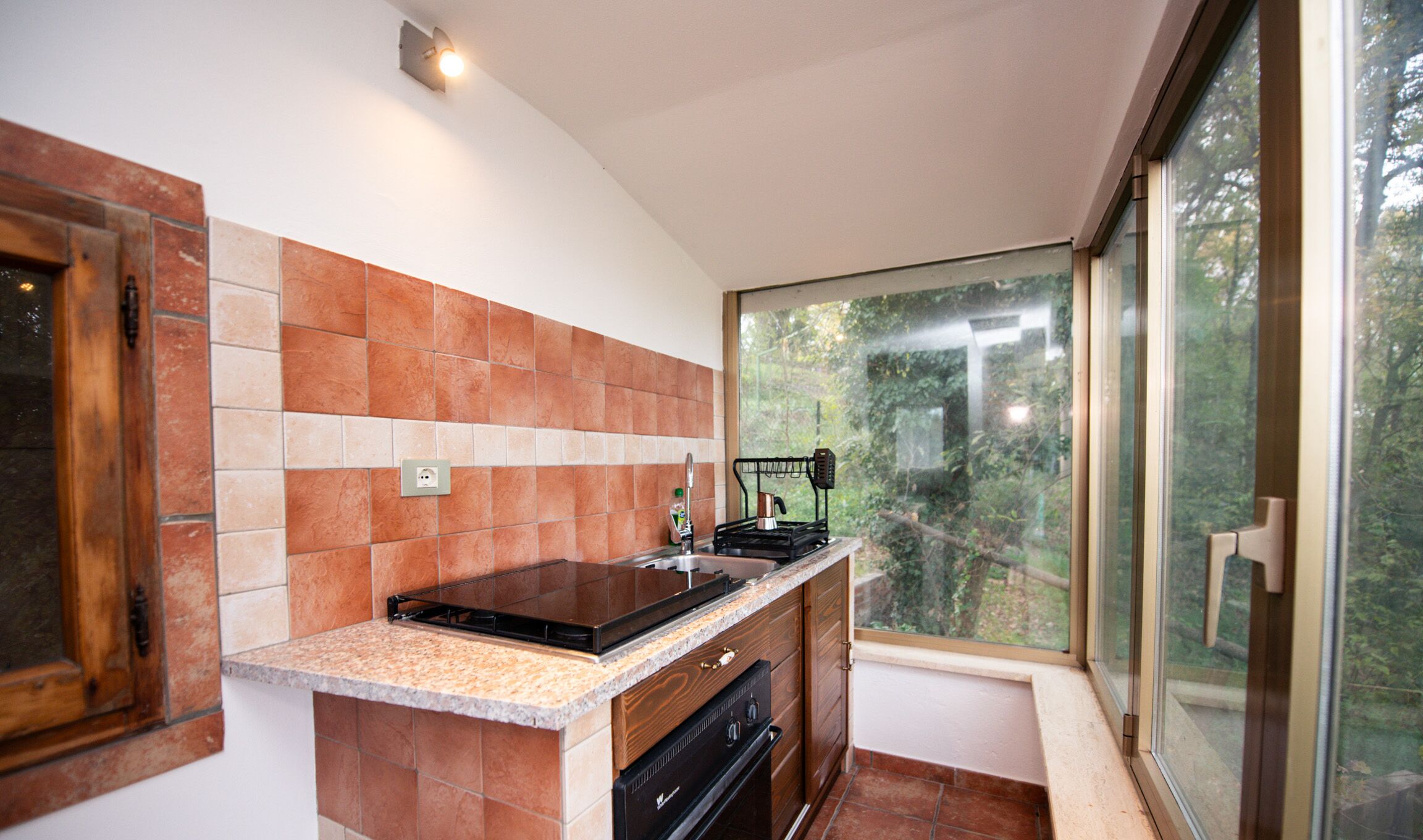 A kitchen with a built-in stove, a window with a view of greenery, and a tiled backsplash.