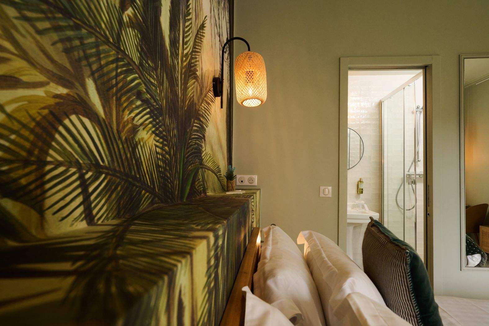 A bedroom with a bed, a wall-mounted lamp, and a door leading to a bathroom with a shower.