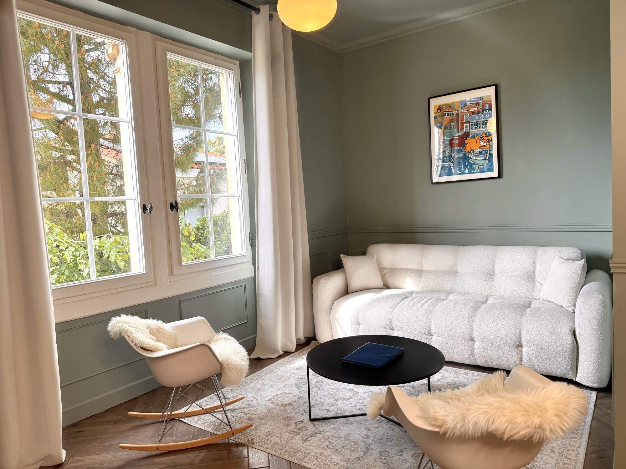 En moderne stue med sofa, gyngestol, sofabord og et stort vindue med gardiner.