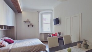 A bedroom with a bed, a desk, a chair, a TV, and a window. - Conte Verde Studio 11 by Wonderful Italy (Turin)
