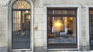 A building facade with a large arched window and a door, featuring a textured stone wall and a number '6' sign. - Conte Verde 10 con Balcone by Wonderful Italy (Turin)