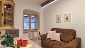 Ein Wohnzimmer mit braunem Sofa, einem Tisch mit roten Tassen, einem Topfpflanzen und einem Fenster mit Aussicht.