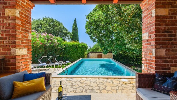 A pool area with a stone patio, wicker furniture, and a bottle of wine.